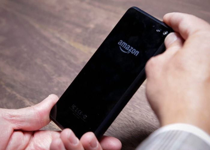 A person holding an Amazon Fire Phone with two hands and a wood desk in the background.