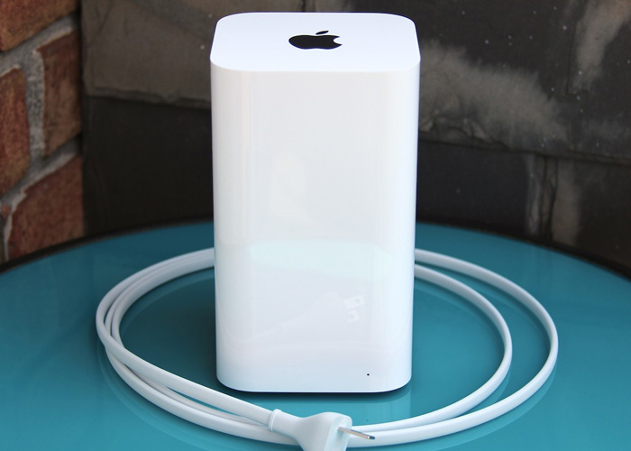 An Apple AirPort Extreme router sits on a blue desk in front of a brick wall
