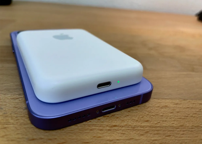 A MagSafe battery pack its on top of a purple iPhone. They both sit on top of a wood desk