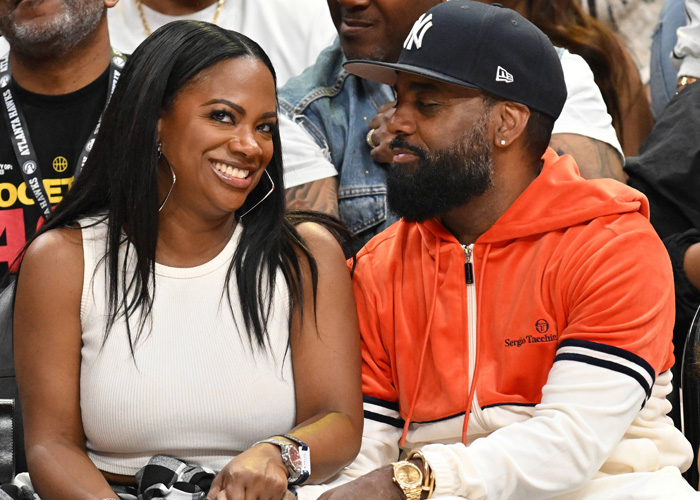 Kandi Burruss and Todd Tucker smiling together in their courtside seats at an Atlanta Hawks basketball game.