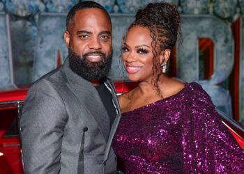 Todd Tucker wearing a grey blazer and Kandi Burruss wearing a sparkly purple sequin dress posing together in front of a classic red car.