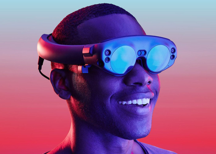 A black man wearing a Magic Leap 1 with a red and blue background in the distance.