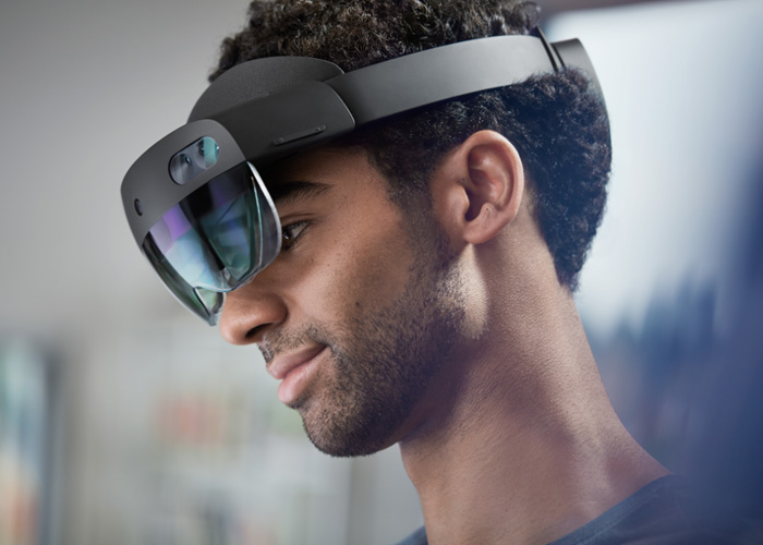 A black man wearing a black Microsoft HoloLens 2 as he stares off to the left.