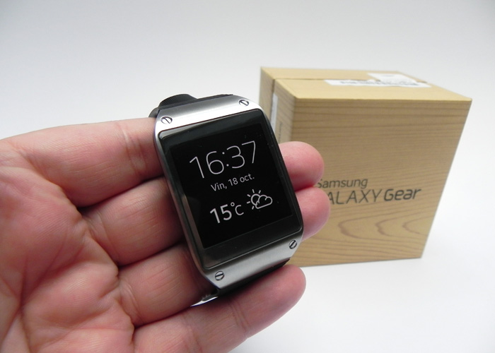 A person holding a Samsung Galaxy Gear watch with the wood packaging in the background.
