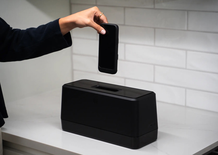 A person placing a phone inside of the black Swippitt toaster like device in the kitchen. 