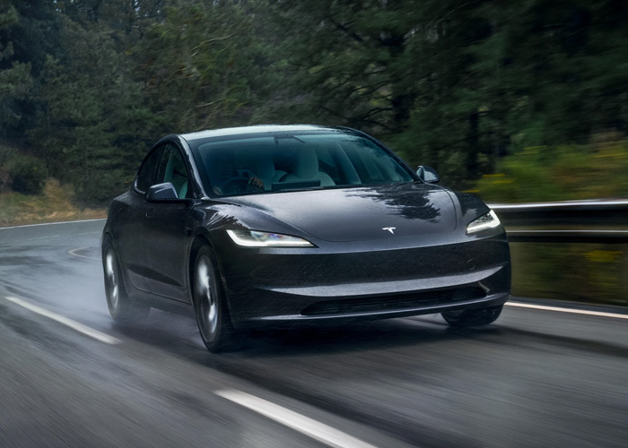 A gray 2026 Tesla Model 3 driving fast on a wet road and water splashes about 